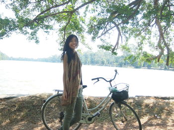 Portrait of young woman standing by bicycle against trees