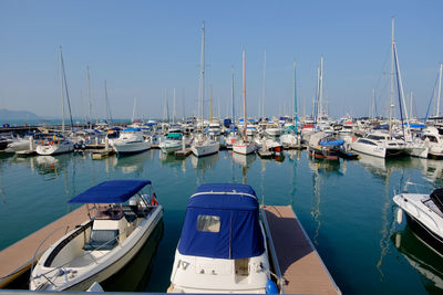 Sailboats moored at harbor against clear blue sky