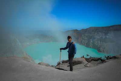 Young man standing on mountain against blue sky