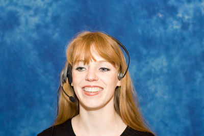 Close-up of young businesswoman using headset against blue background