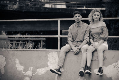 Portrait of young couple sitting on retaining wall