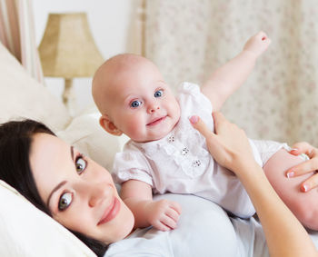 Portrait of cute baby lying on bed with mother at home