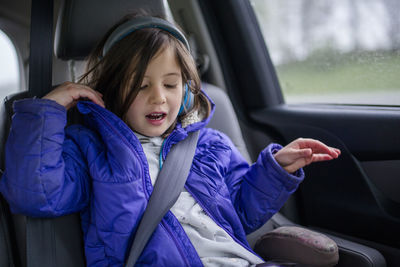 A little girl listens to music on headphones in a car on a car trip