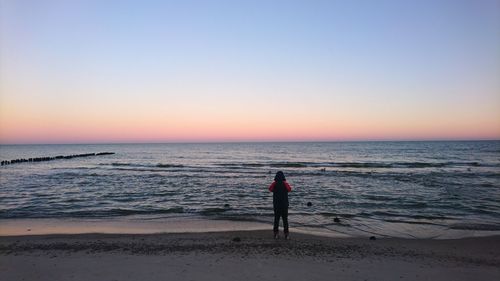 Rear view of person standing against sea during sunset