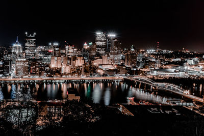 Illuminated buildings by river against sky in city at night