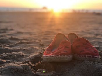 Close-up of shoes on sand at beach against sky during sunset