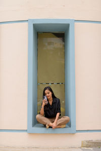 Portrait of young woman sitting against window