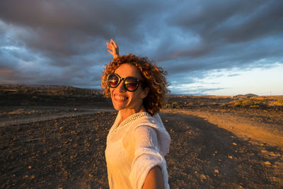 Portrait of young woman wearing sunglasses standing on beach against sky