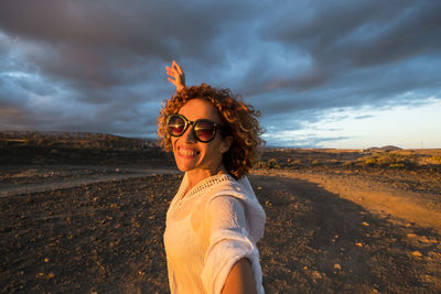 Portrait of smiling mature woman gesturing towards cloudy sky