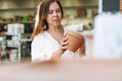 Brunette middle aged woman in white dress buys clay flower pots at hardware store, selective focus
