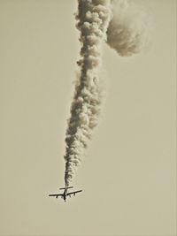 Low angle view of airplane emitting smoke in clear sky