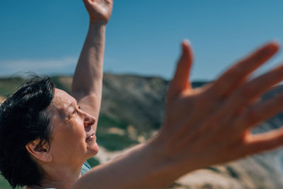 Close-up portrait of an adult woman on a mountain with a smile on her face, raising her hands to the