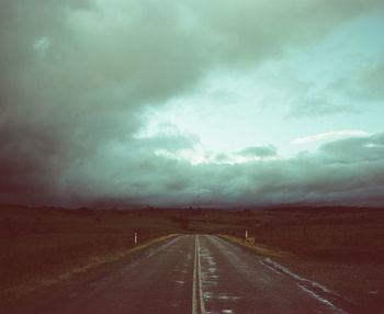 Empty road amidst landscape against cloudy sky