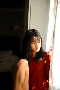 Young woman looking down while sitting on window at home