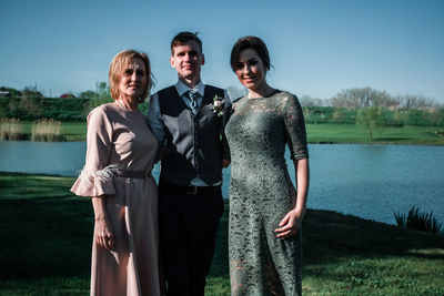 Portrait of friends standing by lake against sky