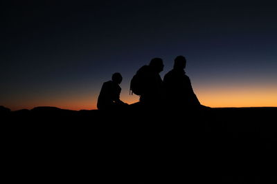 Silhouette people on landscape against sky during sunset