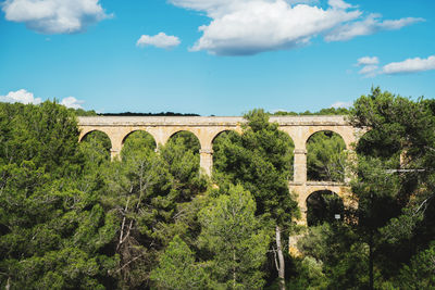 Arch bridge by trees against sky