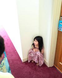 High angel view of girl crouching in corner at home