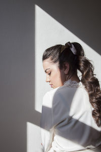 Girl looking away while standing against white wall