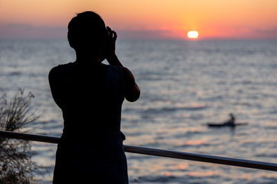 Silhouette woman standing against sea during sunset