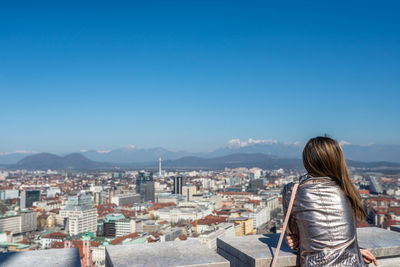 Rear view of woman looking at cityscape against blue sky