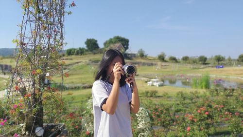 Young woman photographing through binoculars while standing against trees