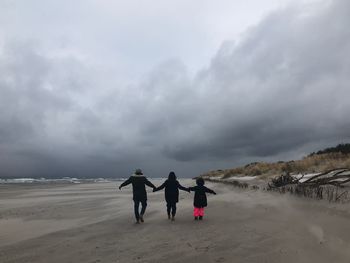 Rear view of family walking on sand at beach during winter