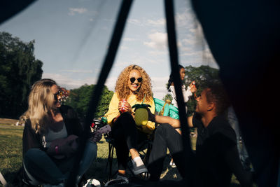 Smiling friends enjoying drinks and music seen through tent at concert