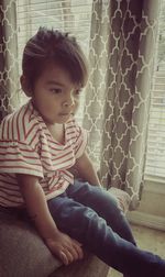 Girl looking away while sitting on window at home