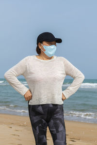 Woman wearing mask standing against sea and sky