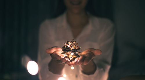 Midsection of woman holding illuminated pine cone in darkroom