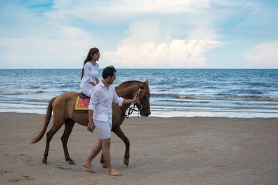 Young woman with boyfriend riding horse at beach