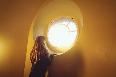 Low angle view of woman standing against illuminated window