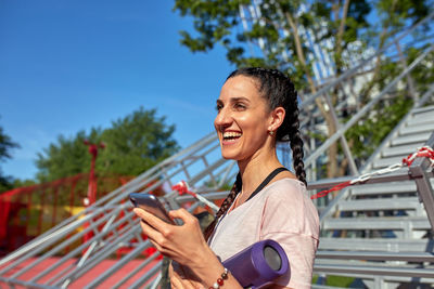 Portrait of smiling young woman using mobile phone against sky