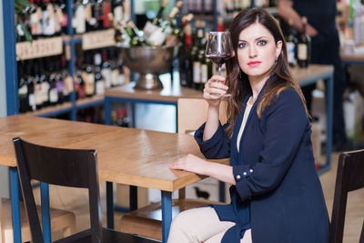 Portrait of young woman with wine glass sitting on table