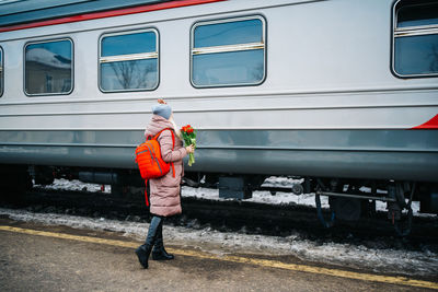 Girl with a red backpack and flowers waves to a departing train