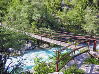 Footbridge over stream amidst trees in forest