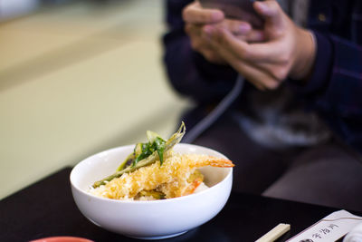 Midsection of person with cooked shrimps in bowl on table