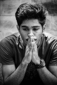 Serious young man with hands clasped sitting outdoors