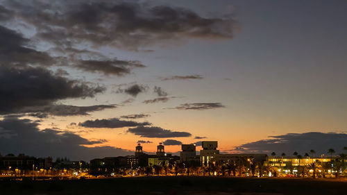 Illuminated buildings in city against sky at sunset