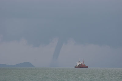 Boat sailing in sea against storm clouds