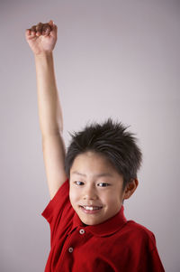 Portrait of smiling boy with hand raised white background