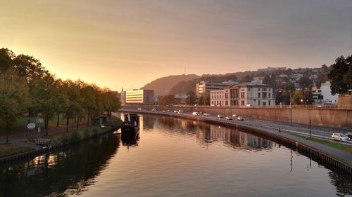 River amidst buildings in city against sky at sunset