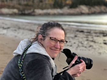 Portrait of smiling woman holding camera at beach