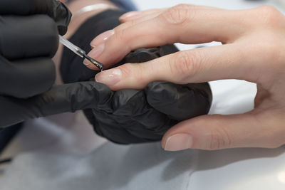 Cropped hands of manicurist applying nail polish on finger of woman