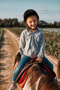 Little smiling girl learning horseback riding. 5-6 years old equestrian in helmet having fun