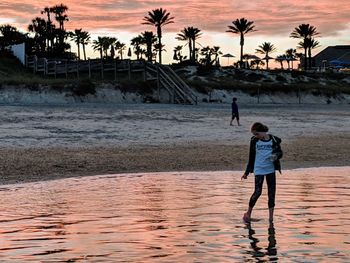 Rear view of women standing at beach during sunset