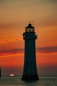 Lighthouse by sea against sky during sunset