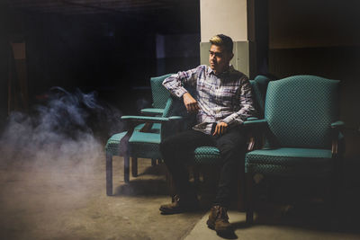 Young man sitting on chair in a smoky basement