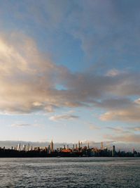 Sea by buildings against sky during sunset